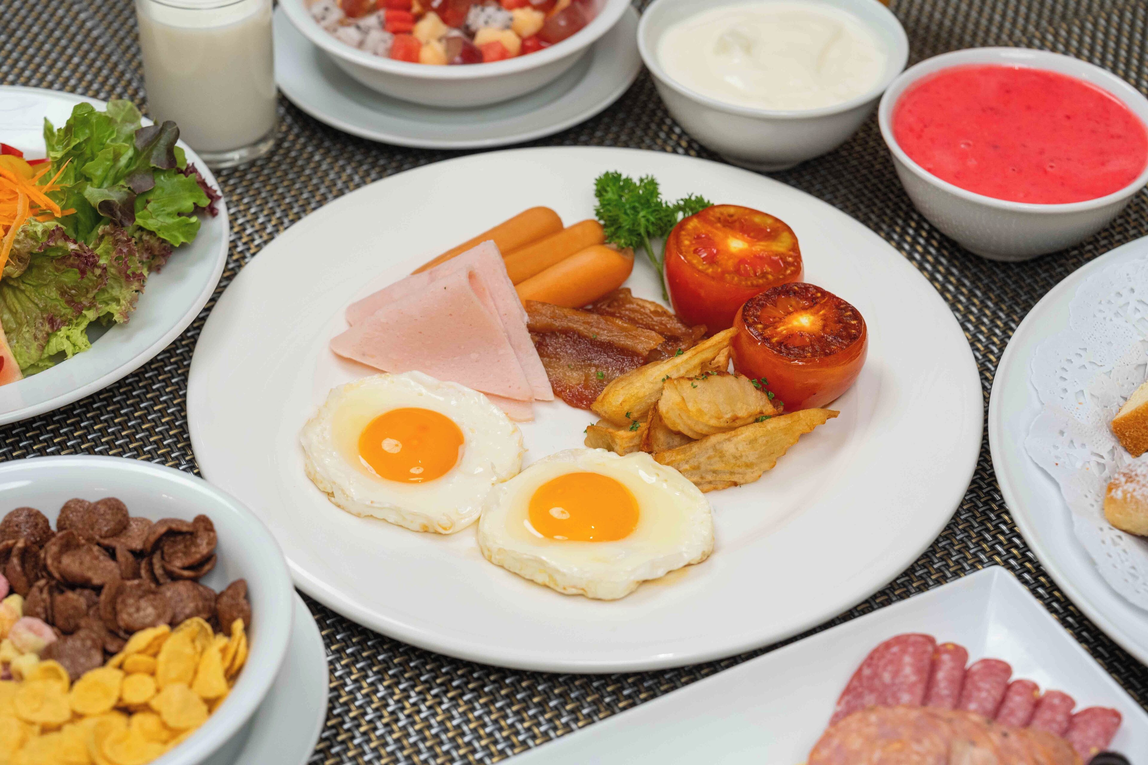 Una mesa de desayuno con platos de huevos, tocino, tomates y diferentes acompañamientos.