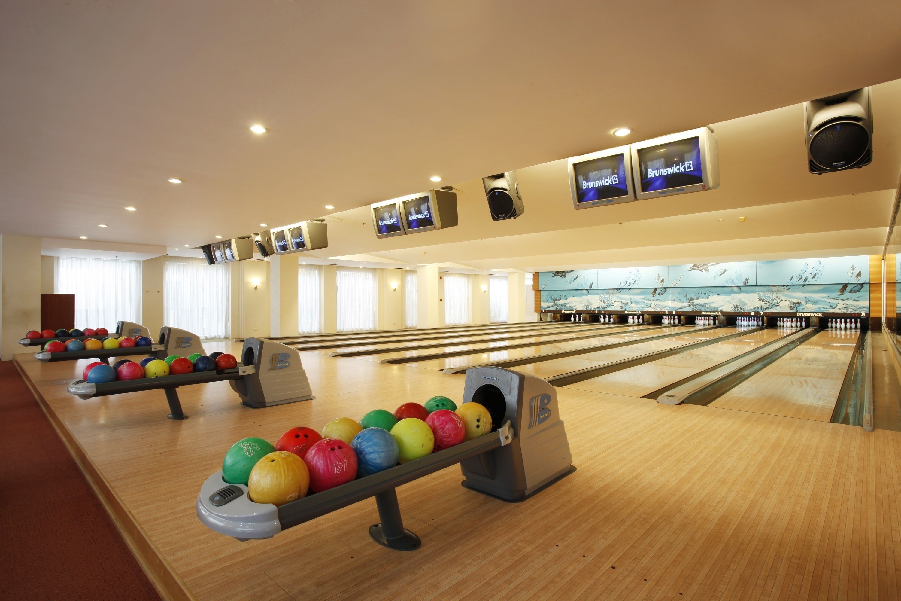 A bowling alley with multiple lanes, a bowling ball return system, and overhead televisions displaying the Brunswick logo.