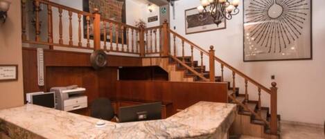 A reception area with a marble counter, wooden staircase, and a chandelier.