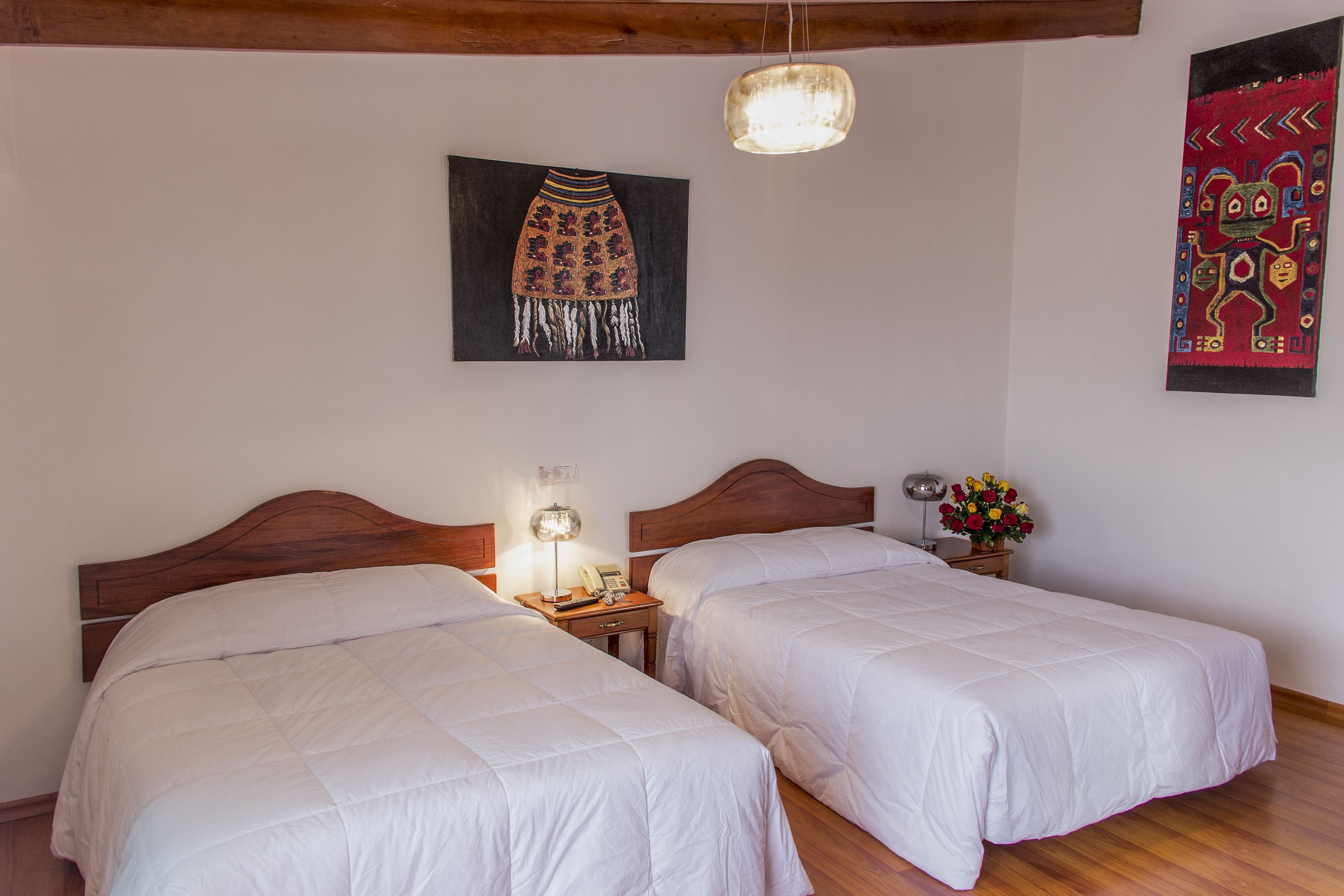 A hotel room with two beds, wooden headboards, a nightstand with a lamp, a telephone, and a wall-mounted artwork.