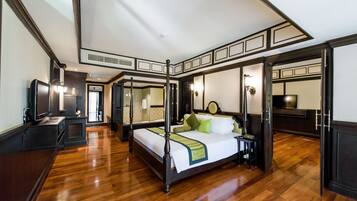 A four-poster bed with a green throw, a television, and a desk lamp in a hotel room with wooden floors and dark trim.