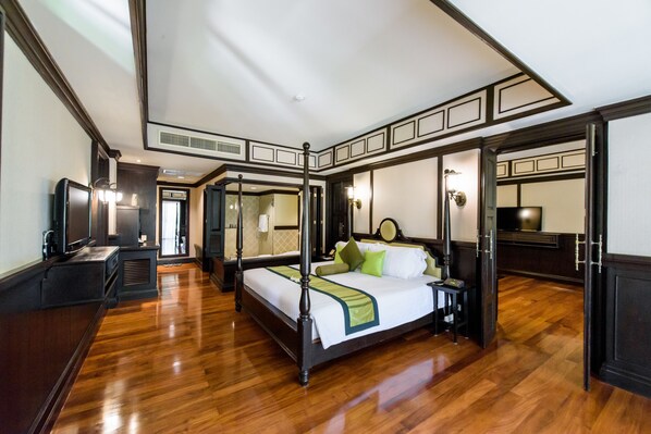 A four-poster bed with a green throw, a television, and a desk lamp in a hotel room with wooden floors and dark trim. - Wora Bura Hua Hin Resort and Spa (Hua Hin)