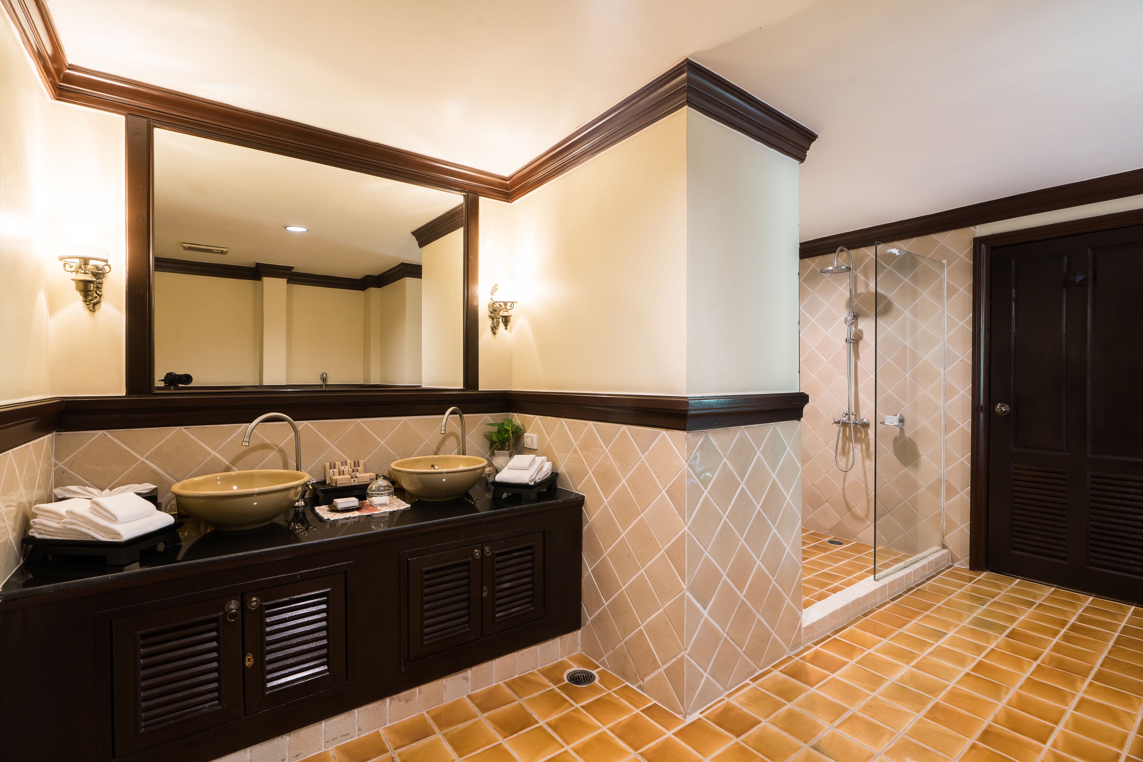 A bathroom with a large mirror, two sinks, a shower, and a dark wooden door.
