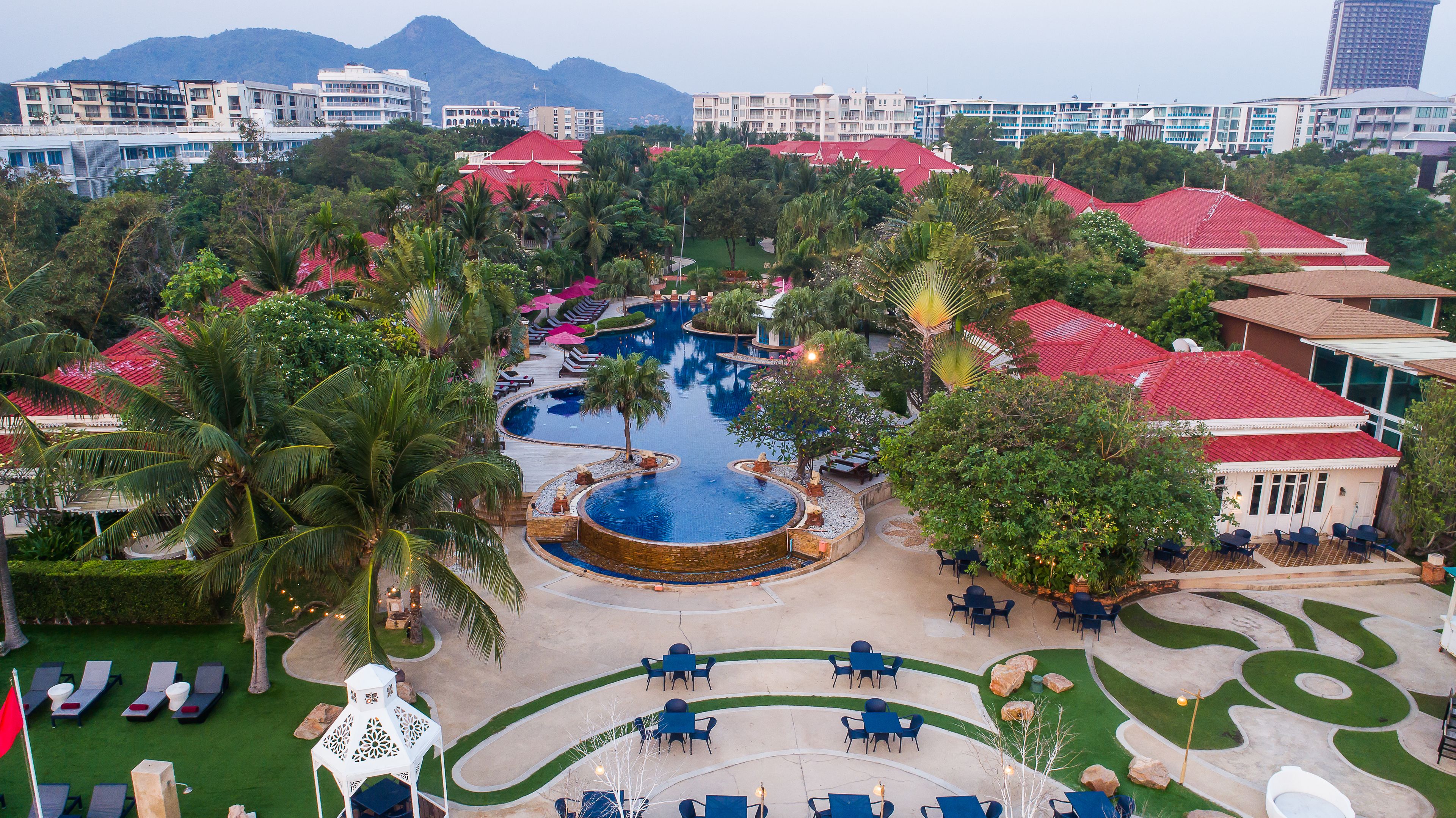 Um resort com piscina central, áreas de descanso e vista para os edifícios ao redor.