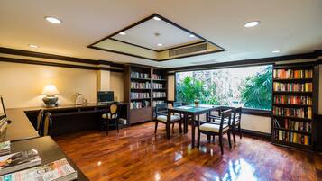 A spacious room with a wooden floor, a dining table with chairs, a bookshelf, and a desk with a lamp.