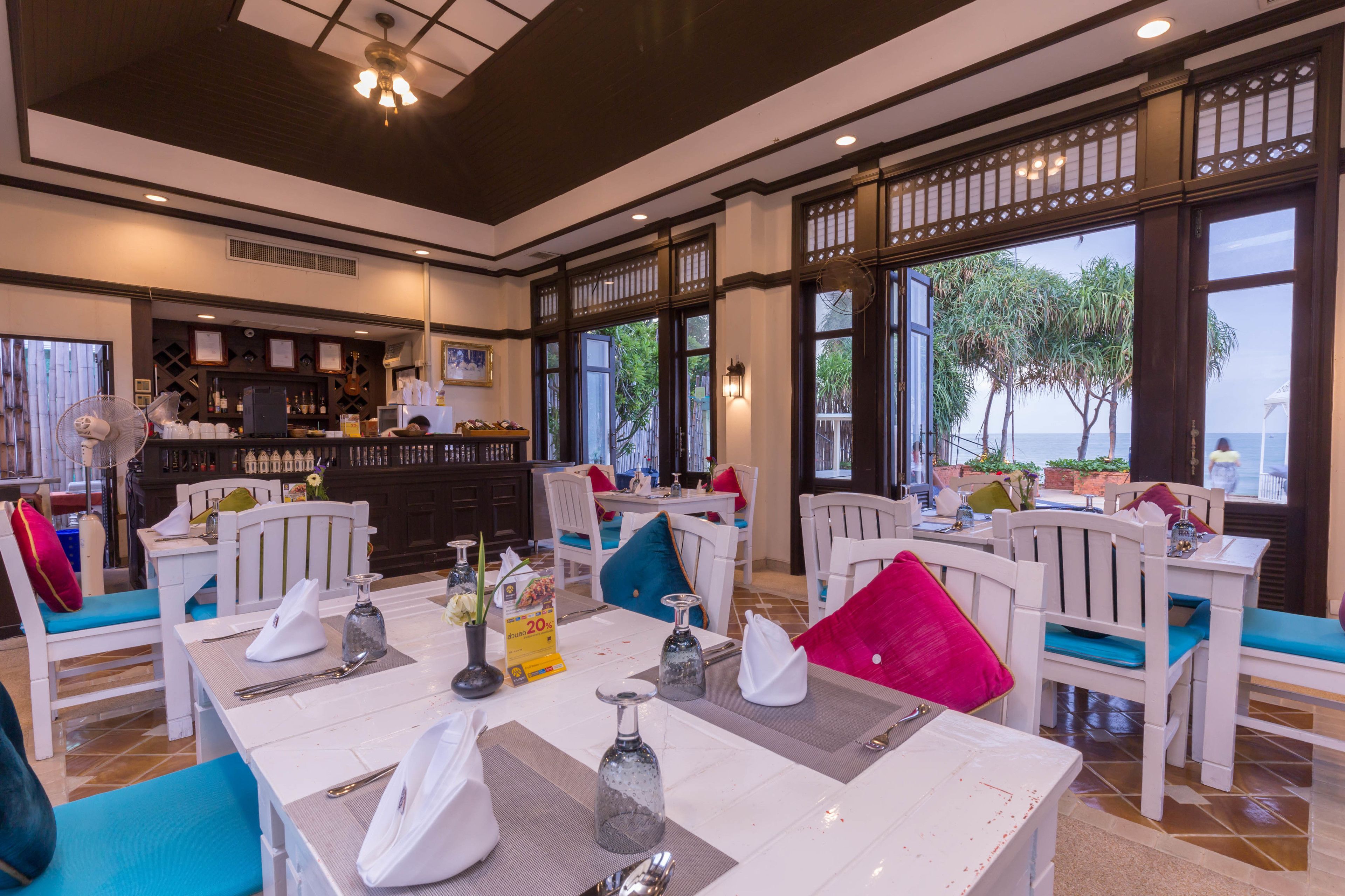 Un restaurant avec des meubles blancs, un coin bar et de grandes fenêtres offrant une vue panoramique.