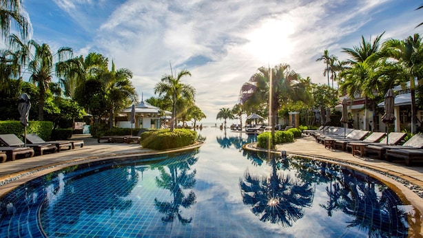A resort pool with lounge chairs and umbrellas, surrounded by palm trees and a clear sky. - Wora Bura Hua Hin Resort and Spa (Hua Hin)