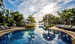 A resort pool with lounge chairs and umbrellas, surrounded by palm trees and a clear sky. - Wora Bura Hua Hin Resort and Spa (Hua Hin)
