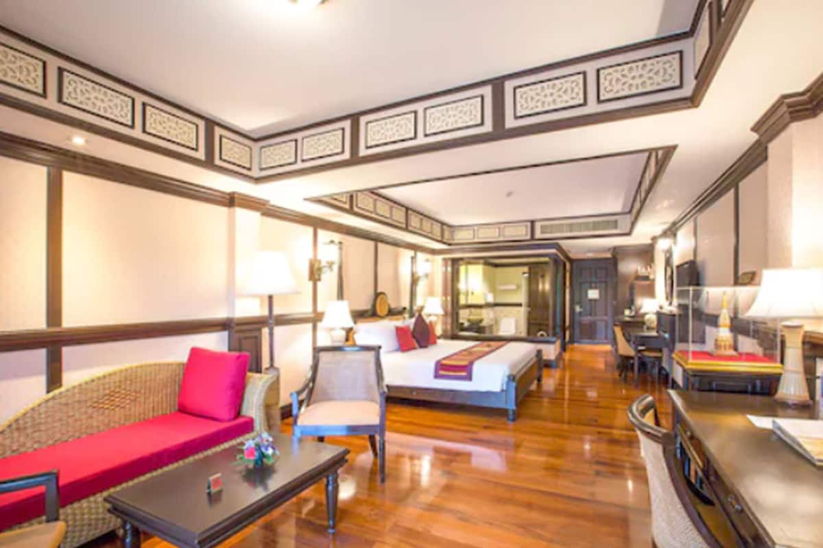 A hotel room with a bed, a sofa, a chair, a table, and a mirror.
