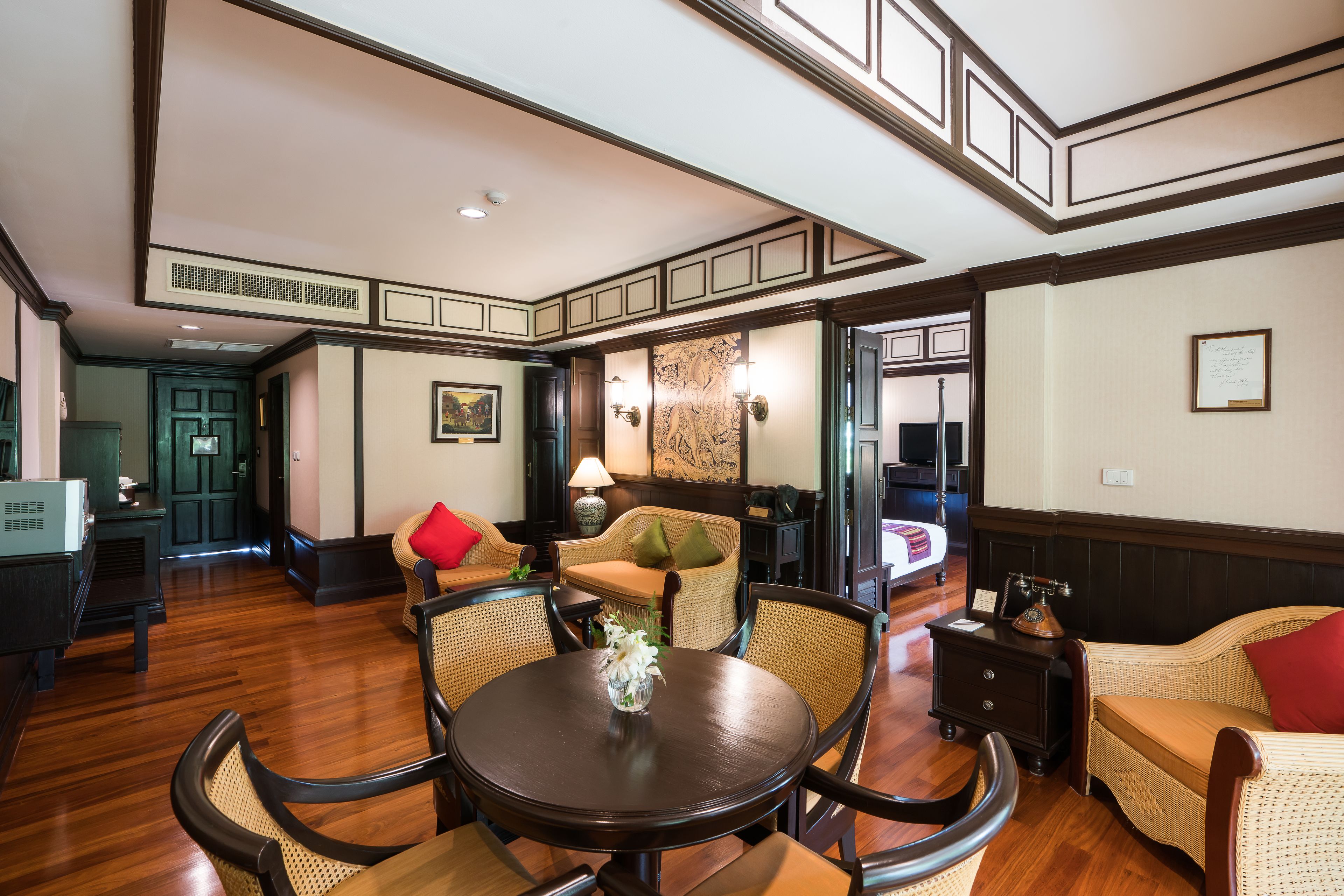 A spacious room with a wooden floor, a round table with chairs, a sofa, and a small side table with a lamp.