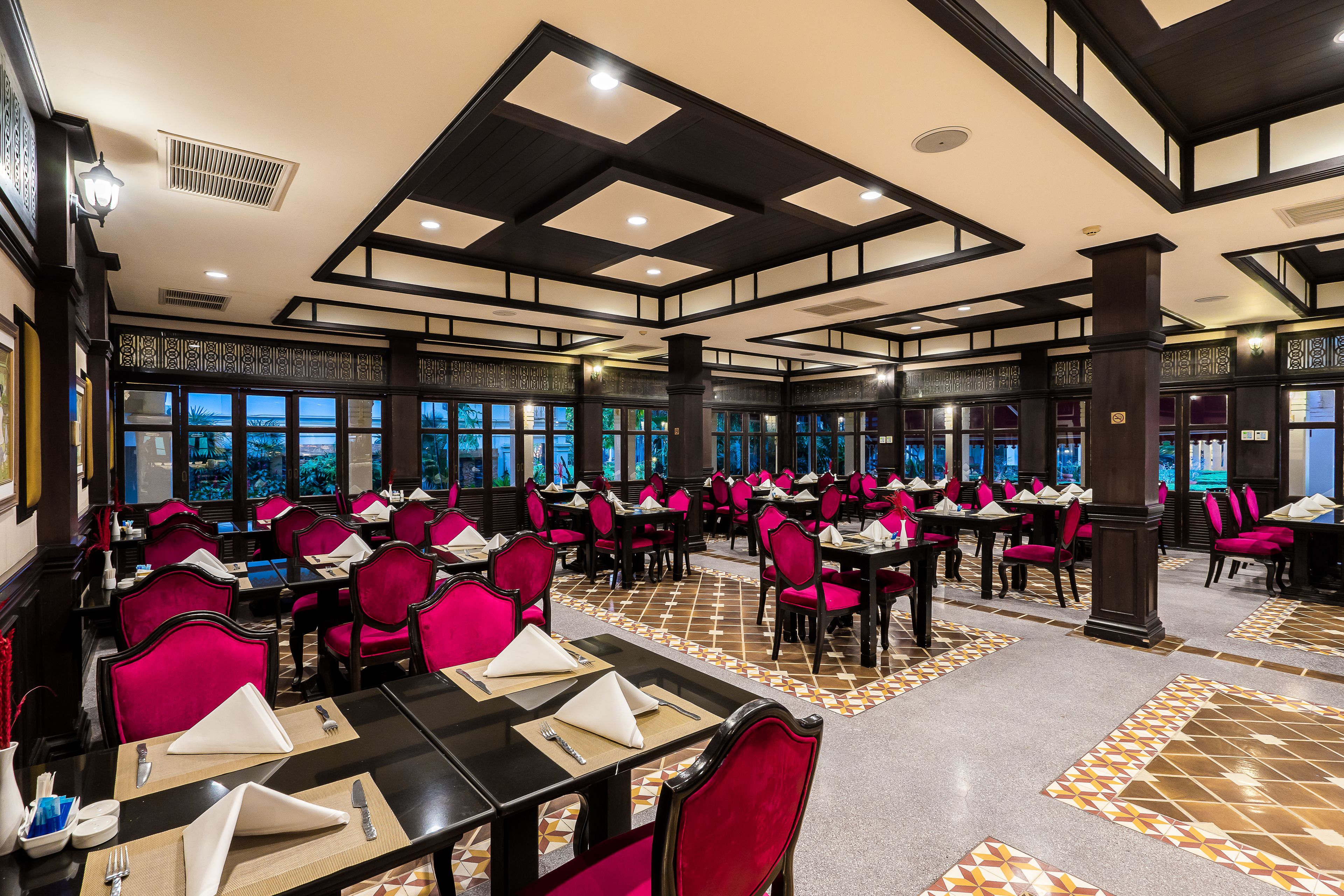 Un vaste espace dédié à la salle à manger, avec de nombreuses tables et chaises, de grandes fenêtres et un sol à motifs.