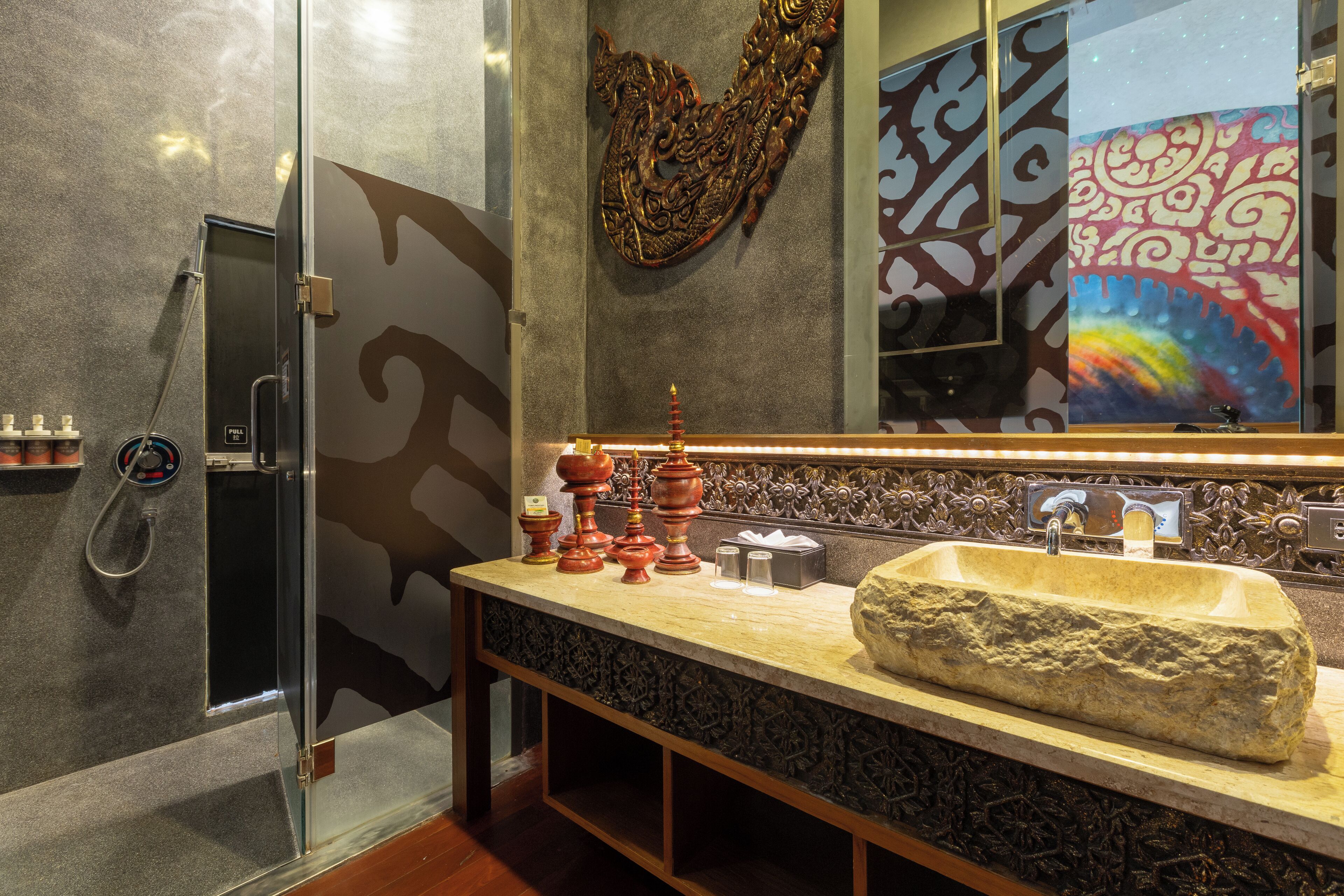 A bathroom with a large stone sink, a glass shower enclosure, and decorative wall art.