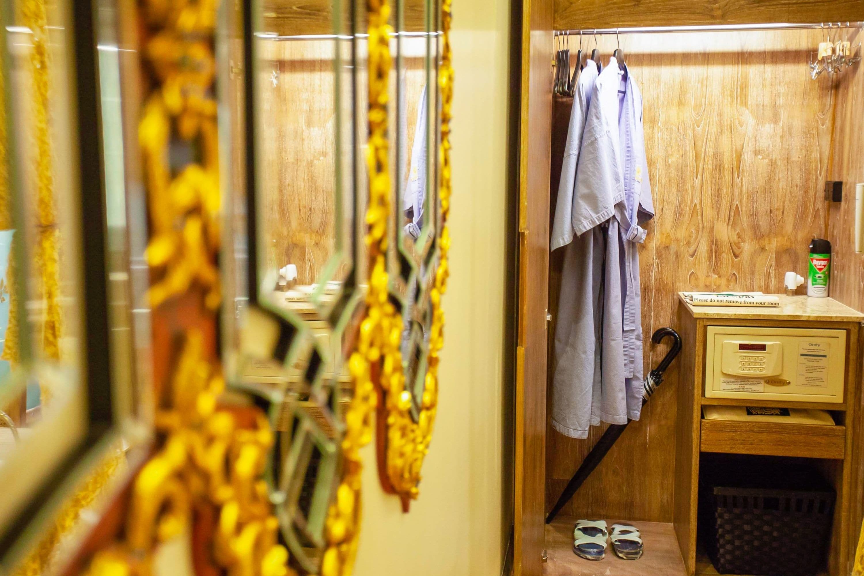 A hotel room with a wooden door, a small table with a bottle, a pair of slippers, and a towel hanging on a hook.