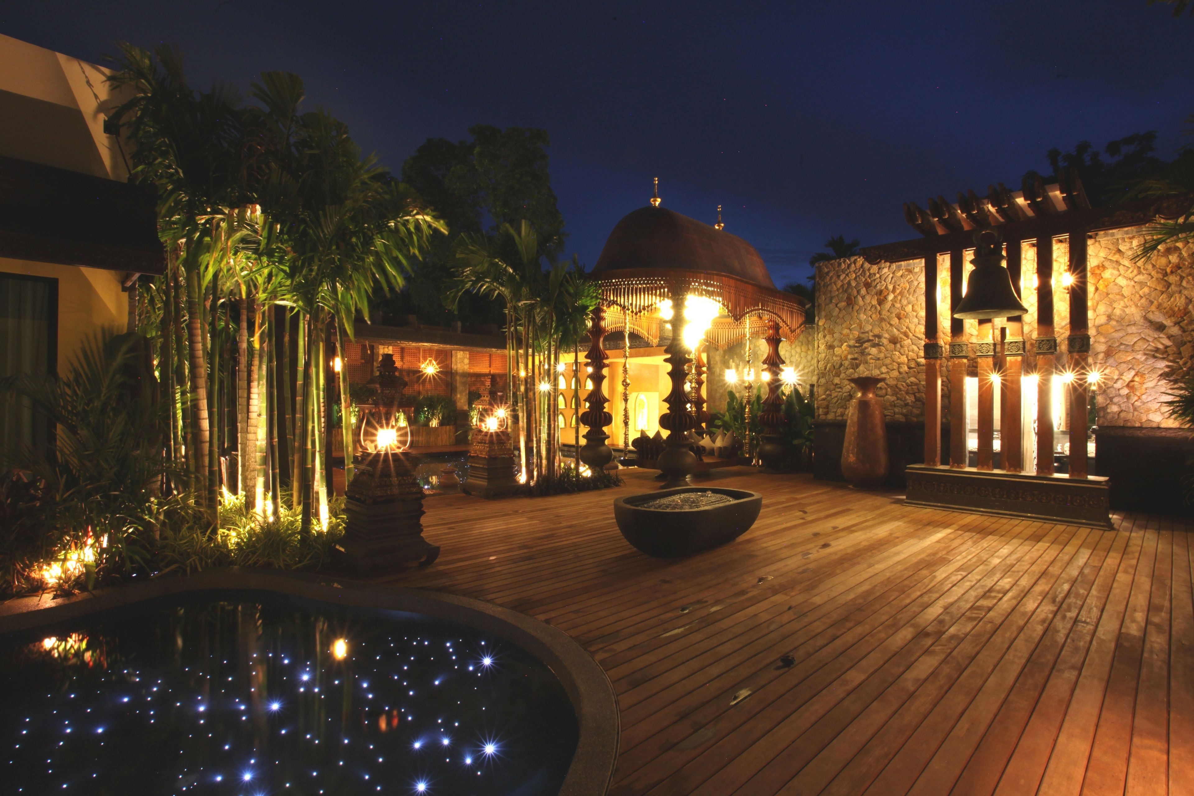 A wooden deck with a fountain, palm trees, and a gazebo with lights.