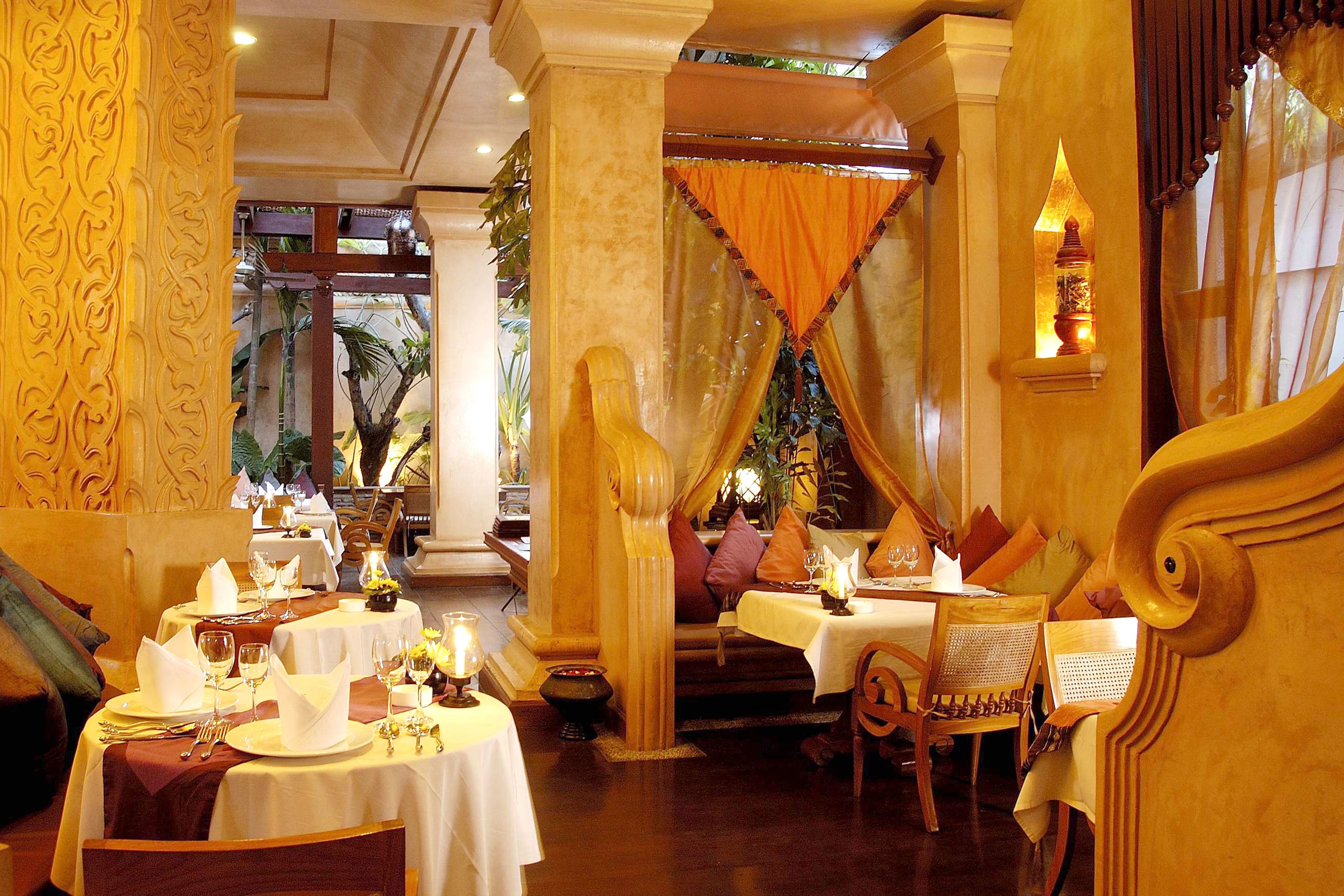A restaurant with ornate columns, tables set with white tablecloths, and a warm interior ambiance.