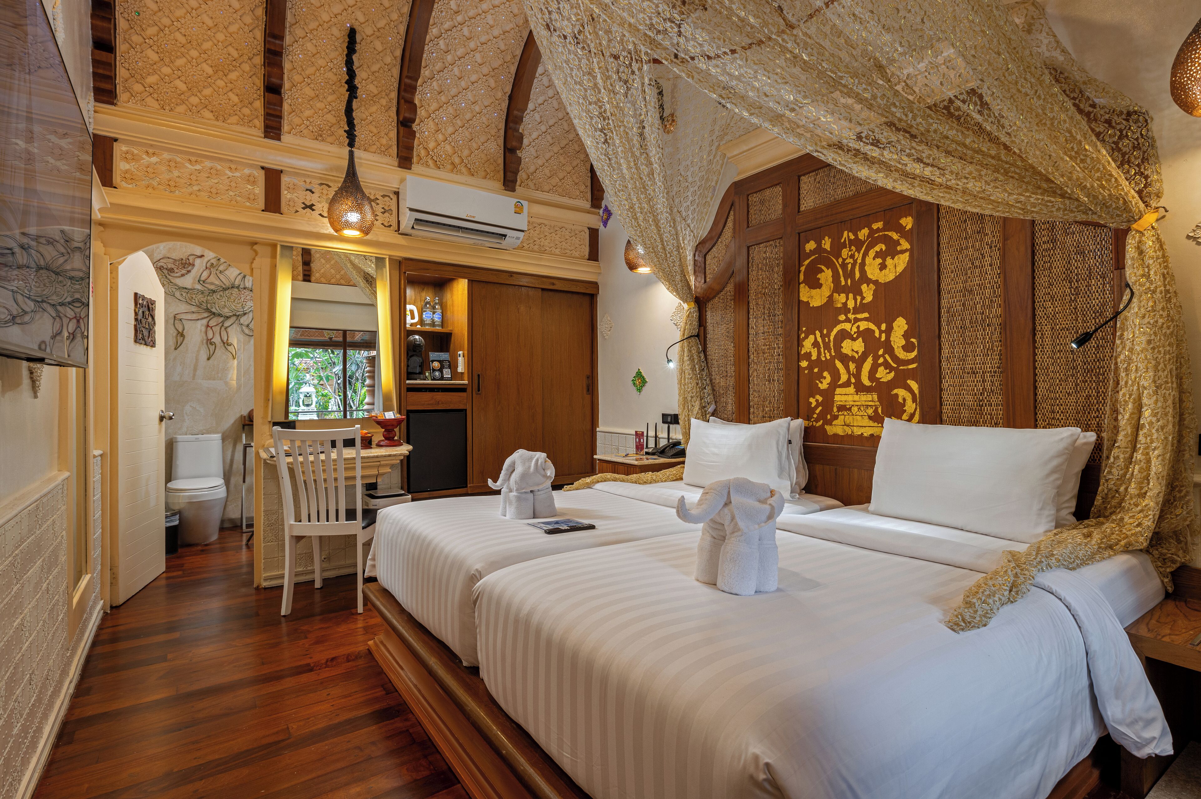 A room with two beds, a wooden desk, and a bathroom.
