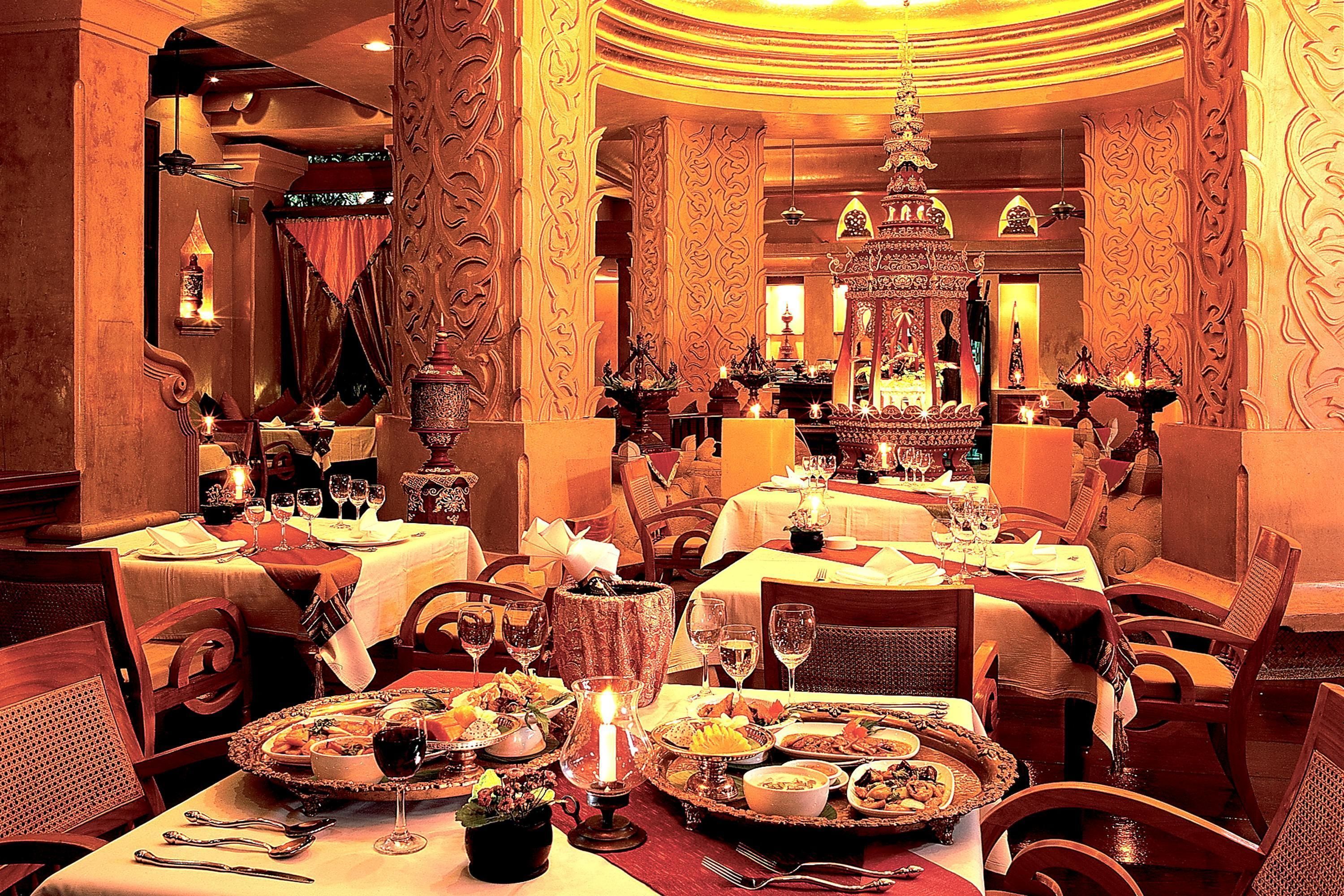 Un comedor lujoso con decoración elaborada, varias mesas dispuestas para comer y una lámpara central.