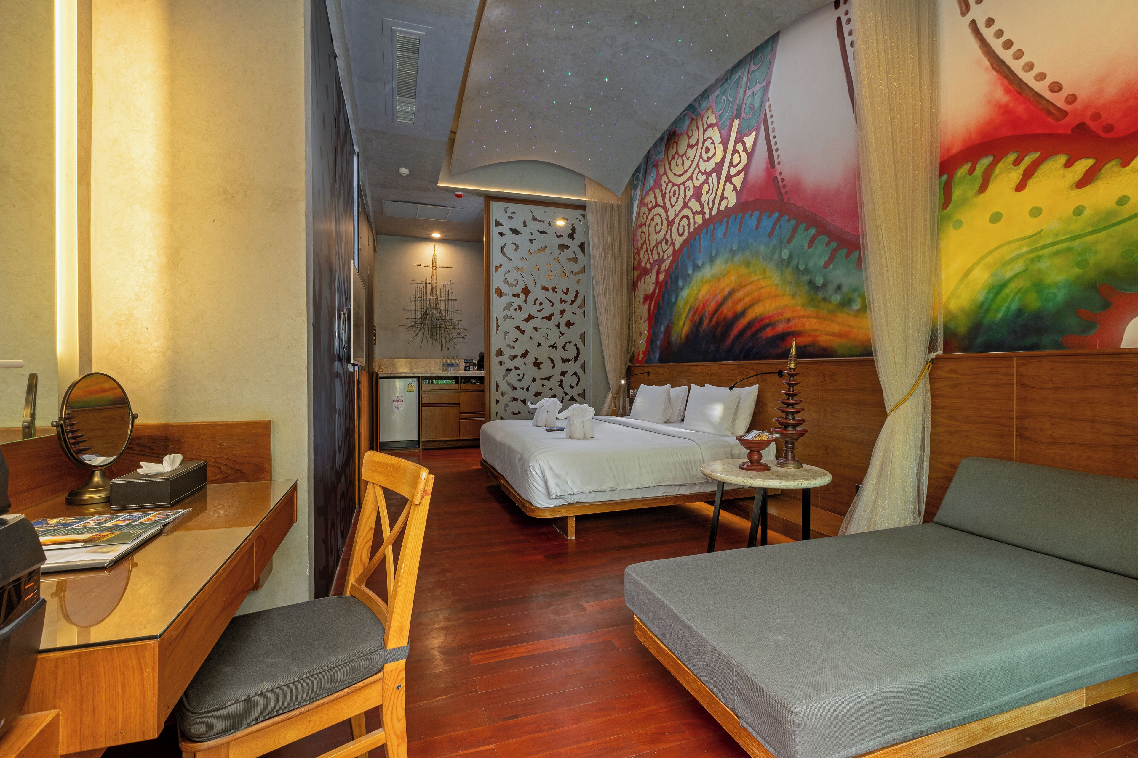 A hotel room with a bed, a sofa, a desk with a chair, and a dining table.
