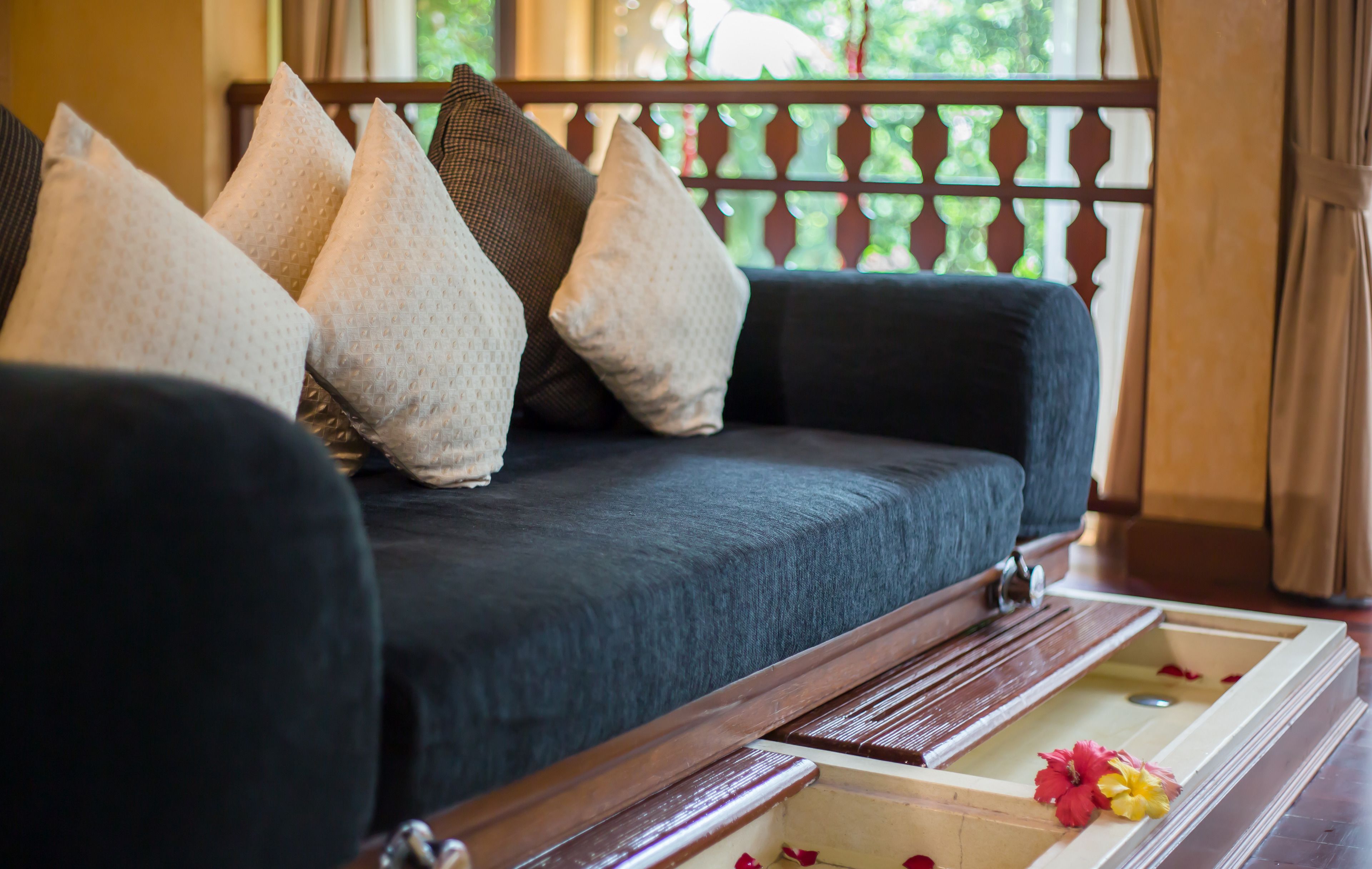 Ein dunkelgraues Sofa mit vielen Kissen und einem Holztablett mit Blumen.