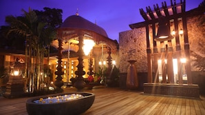 Een binnenplaats met een grote fontein, een houten terras en een gebouw met een koepel en decoratieve verlichting.