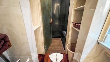 A narrow bathroom with a wooden floor, a white towel on the floor, a wicker basket, and a towel rack.