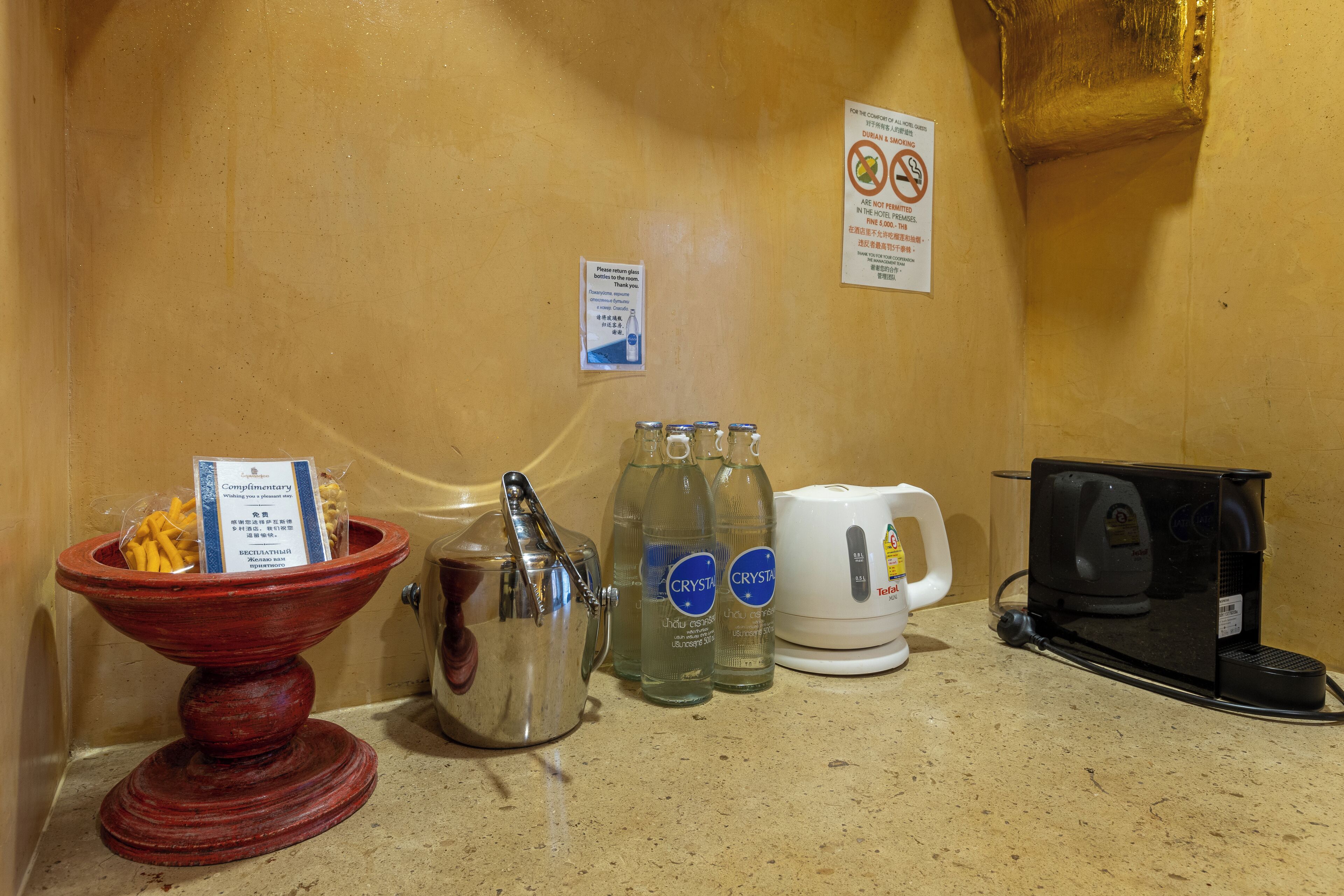 A kitchenette area with a coffee maker, two bottles of Crystal water, a teapot, and a bowl of snacks.
