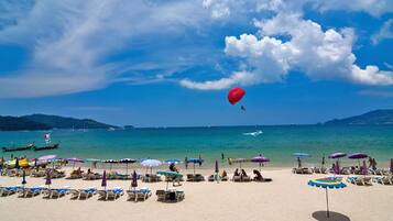 Una spiaggia con file di lettini e ombrelloni, un cielo azzurro limpido e un palloncino rosso che vola.