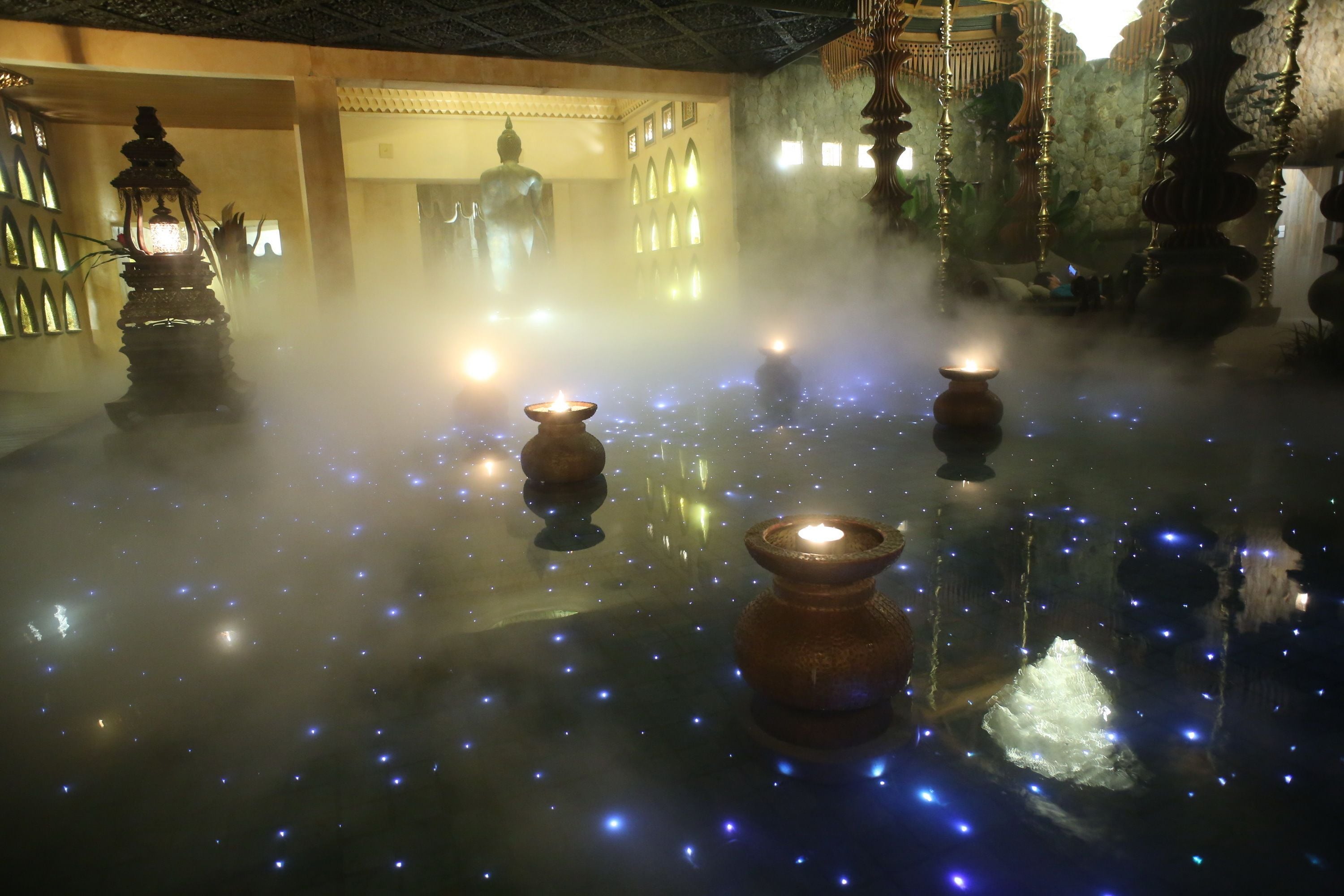 A room with a reflective floor, ornate columns, and a Buddha statue in the background.