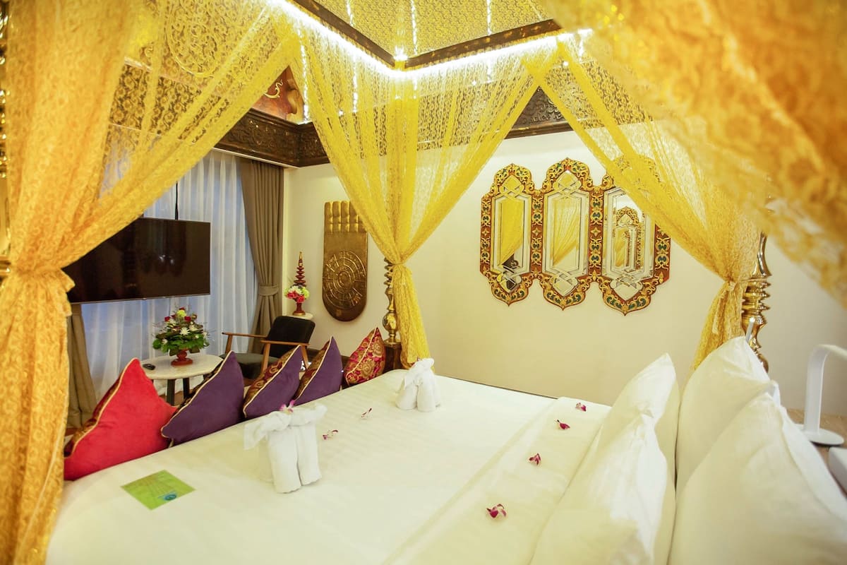Una habitación de hotel con cama, televisión, una mesita con un jarrón de flores y espejos decorativos en la pared.