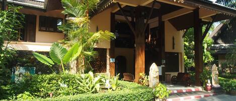 A traditional house with a covered porch, lush greenery, and a statue.
