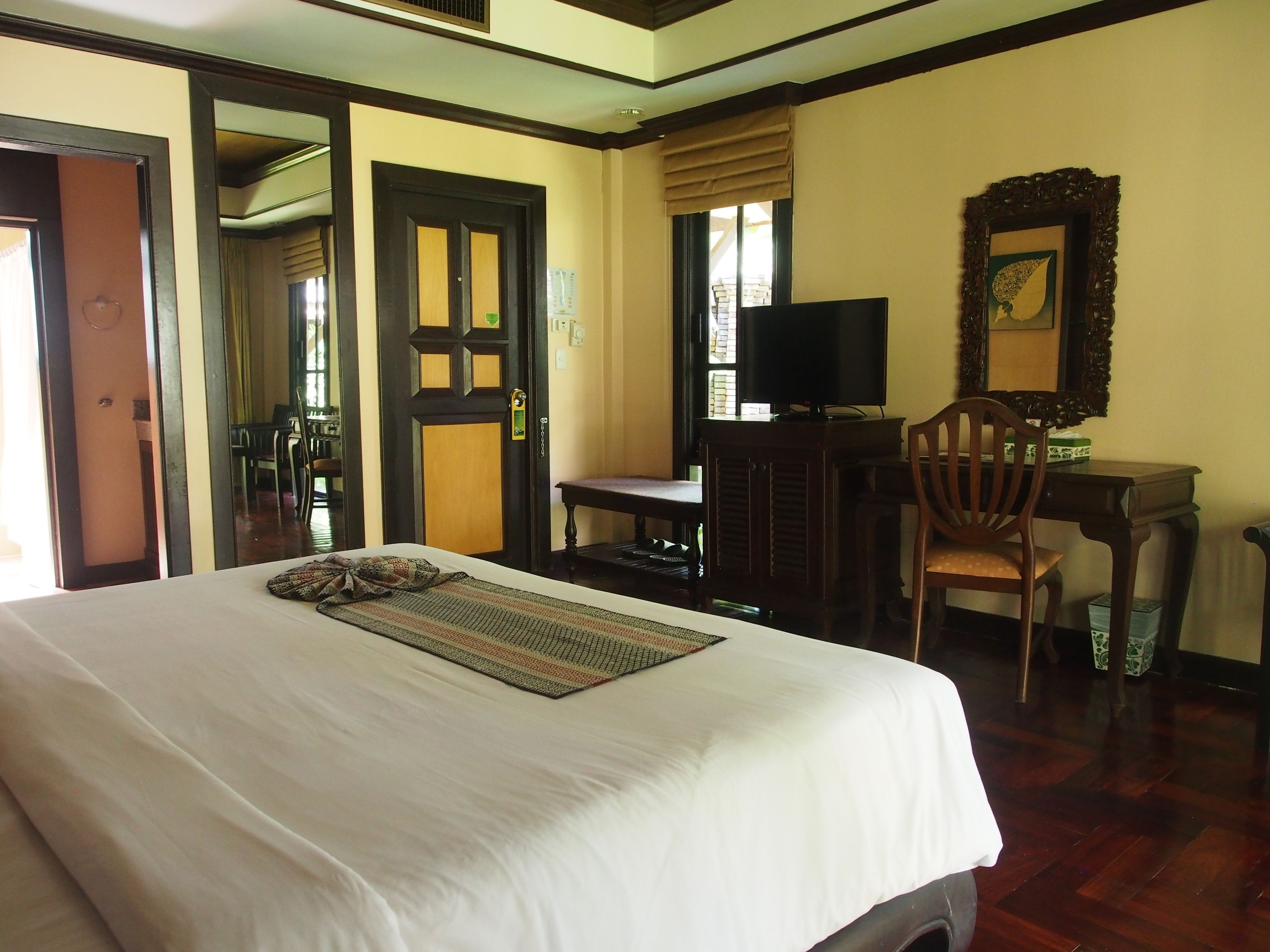 A hotel room with a large bed, a desk with a chair, a television, and a mirror on the wall.