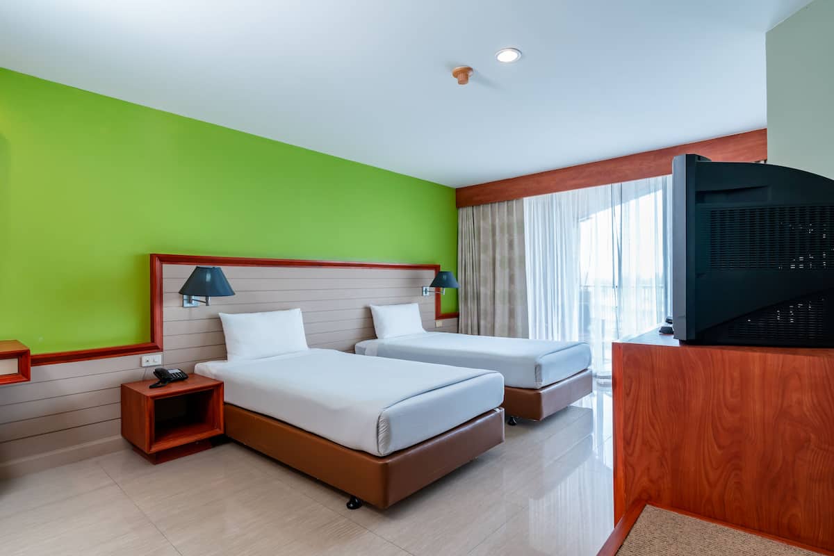 A hotel room with two beds, a TV, a nightstand, and a window with curtains.
