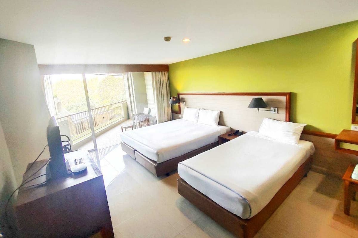 A hotel room with two beds, a desk, a chair, and a balcony with a view.