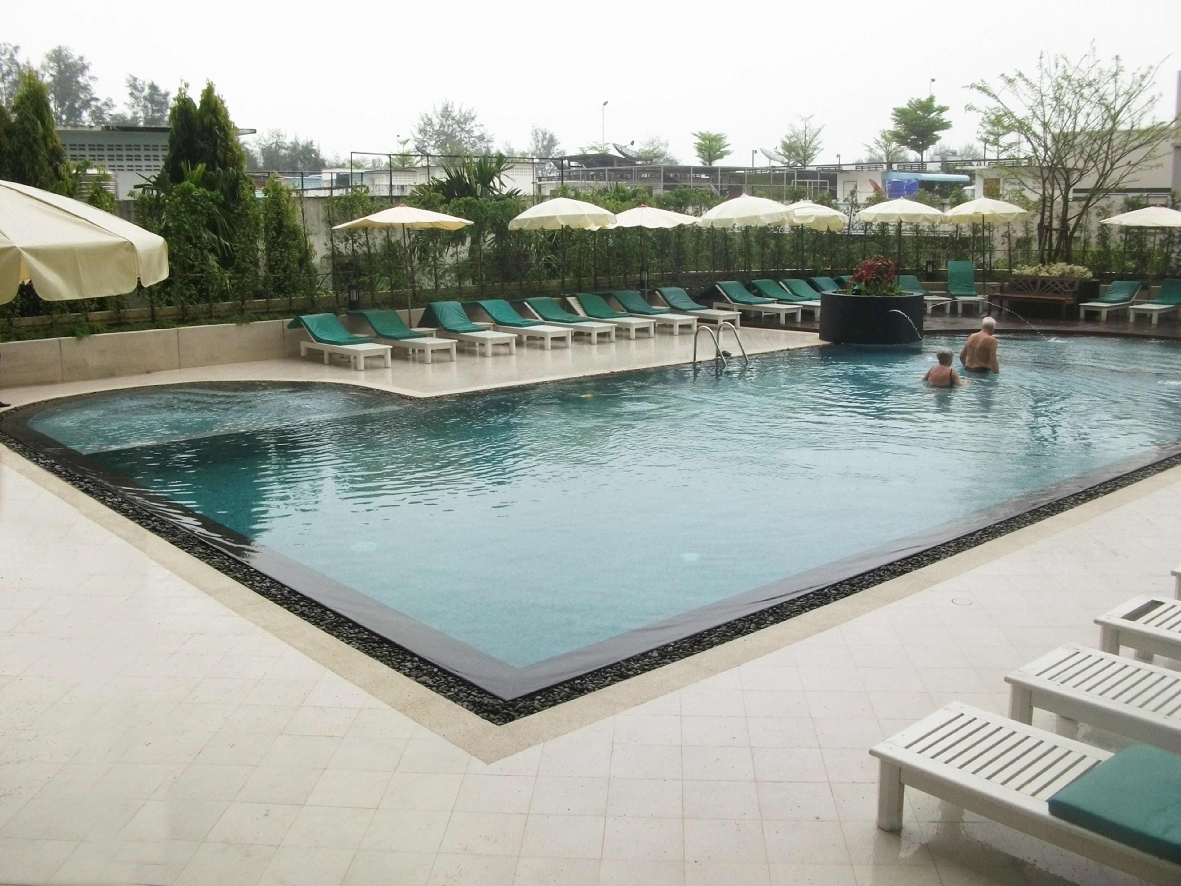 A swimming pool with green lounge chairs and umbrellas.