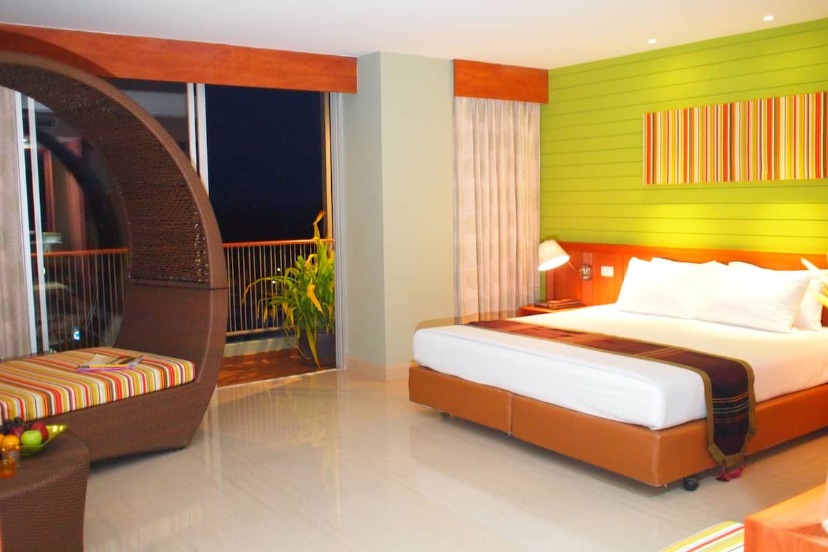 A hotel room with a bed, a balcony with a chair, and a view of the night sky.