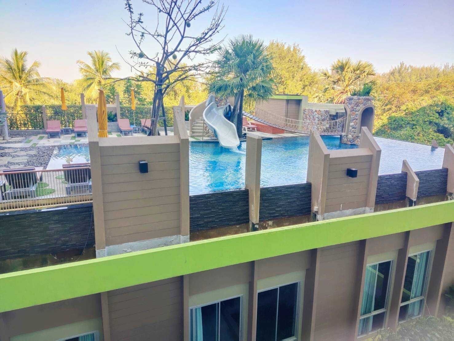 Una piscina en la azotea con un tobogán, rodeada de palmeras y un muro de piedra.