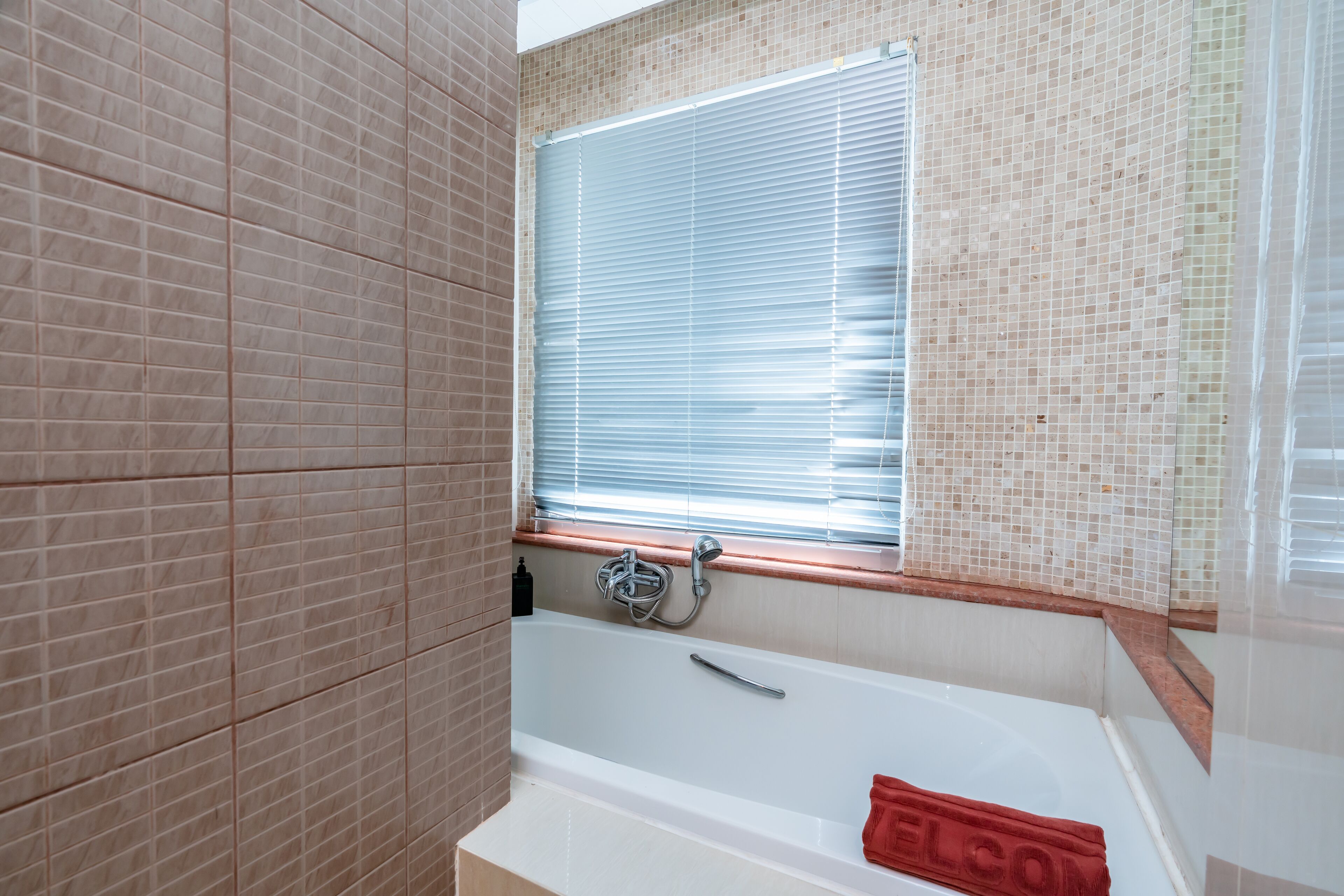 A bathroom with a bathtub, a window with blinds, and a red towel.
