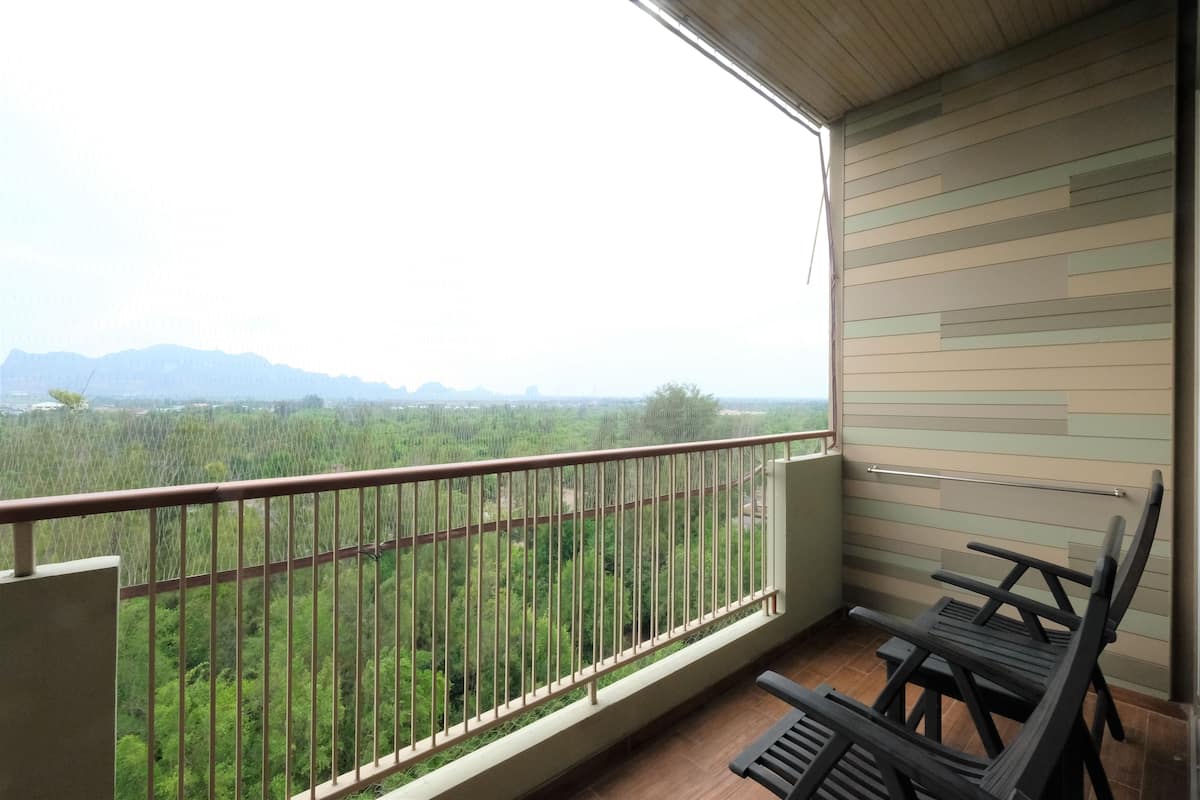 A balcony with a metal railing, a view of a forested area, and two black chairs.