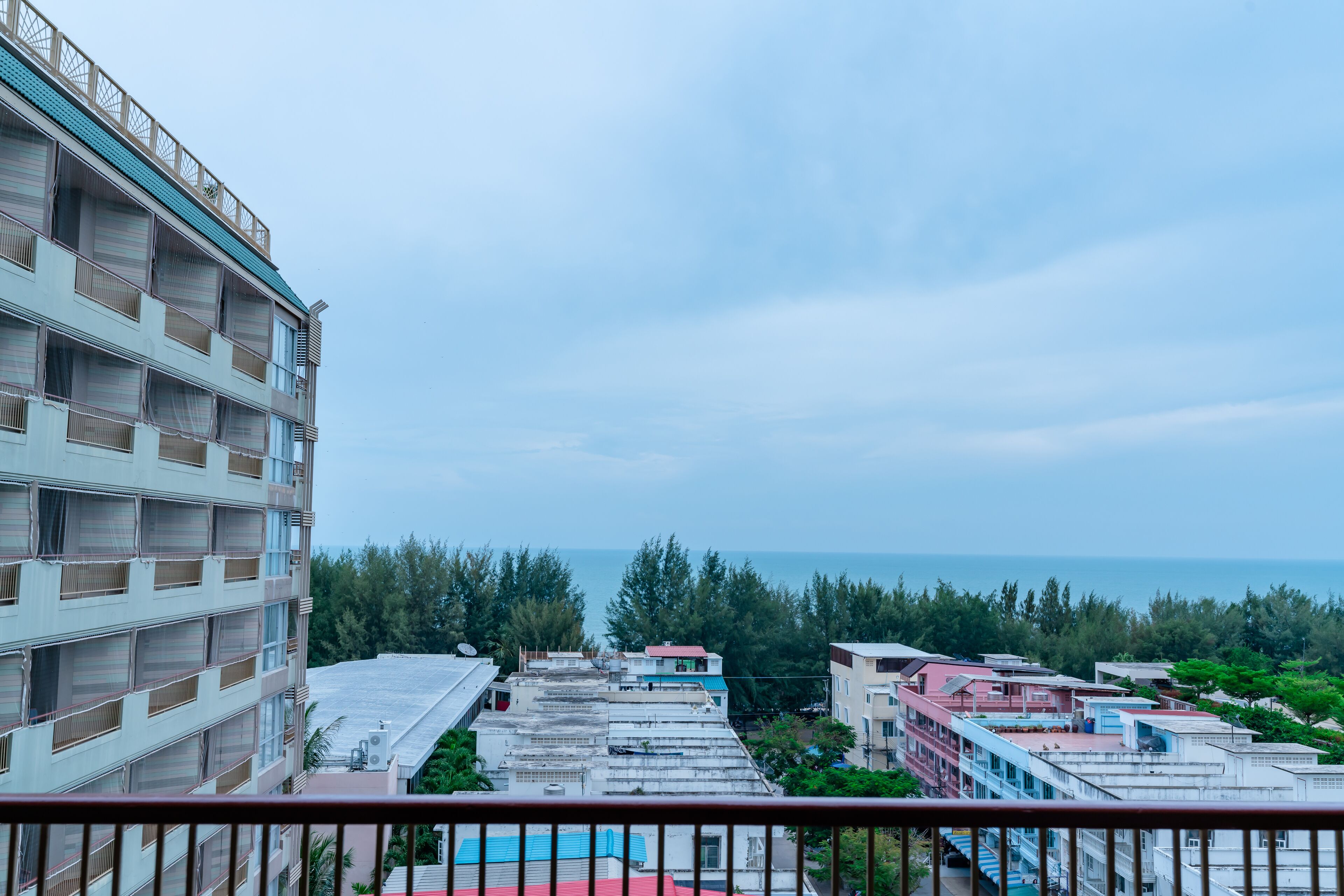 Un edificio de varios pisos con balcones, vista al mar y una combinación de edificios residenciales y comerciales en el fondo.