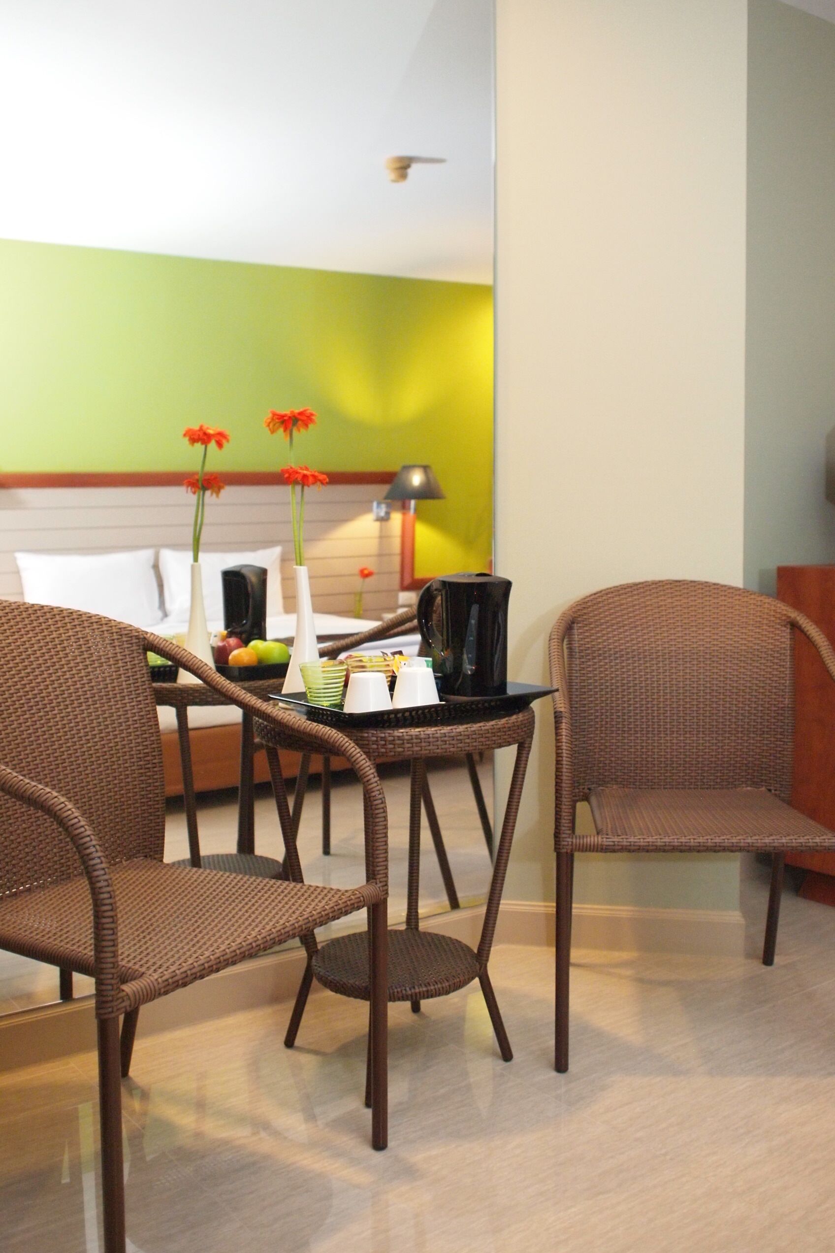 A hotel room with wicker furniture, a bed, a coffee table, and a lamp.