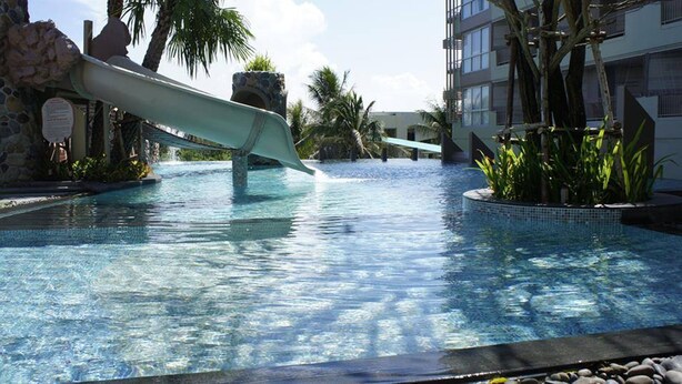 A pool with a slide, palm trees, and a building in the background. - Long Beach Cha-Am Hotel (Cha-am)