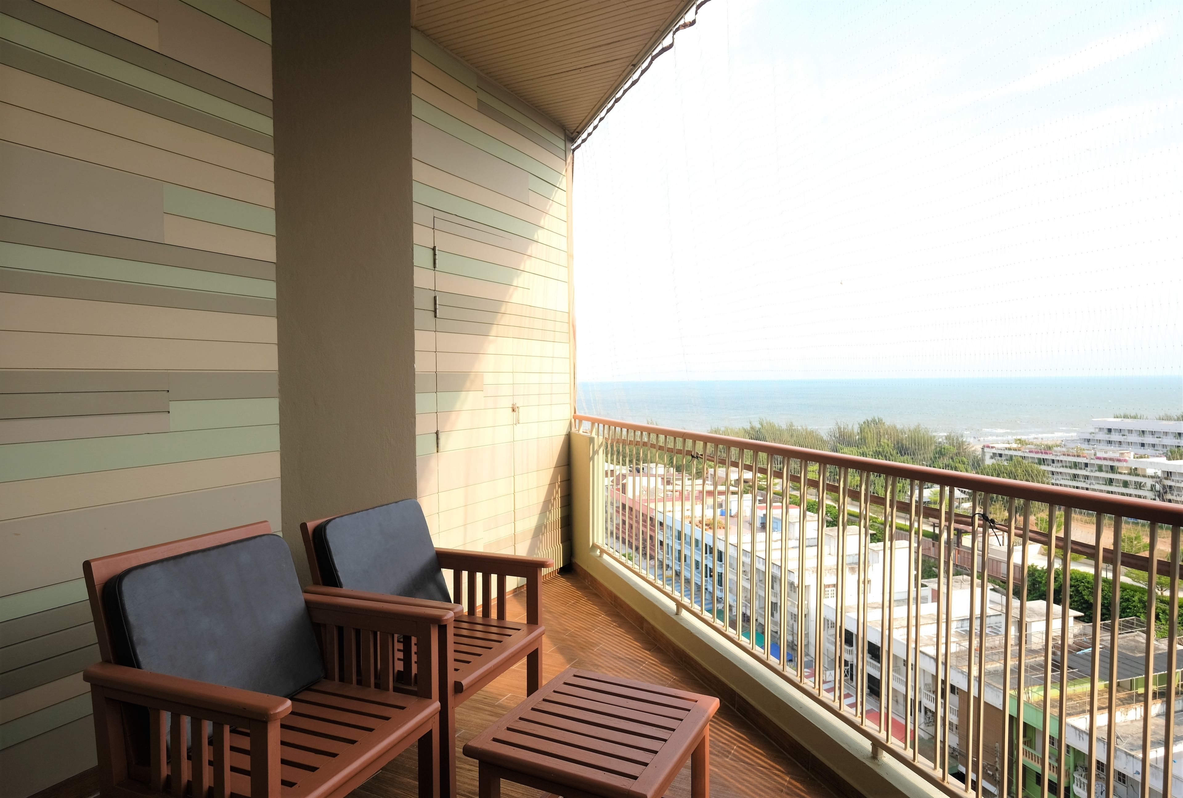 A balcony with two wooden chairs and a small table, overlooking a cityscape and the sea.