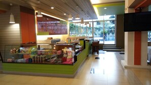 A brightly lit indoor space with a green counter displaying snacks and beverages, a pool bar area, and large windows offering a view of an outdoor swimming area. - Long Beach Cha-Am Hotel (Cha-am)