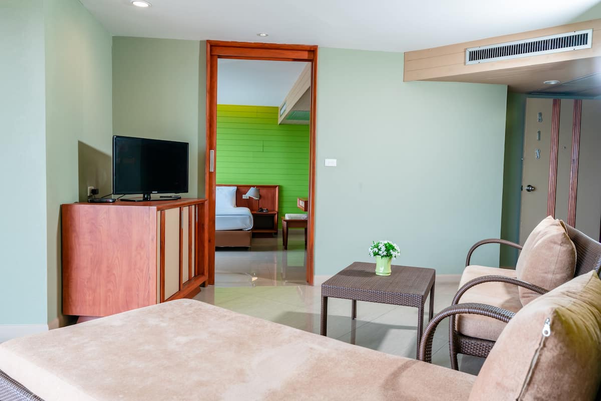 A hotel room with a sofa, a television, a small table with a plant, and a bed in the background.