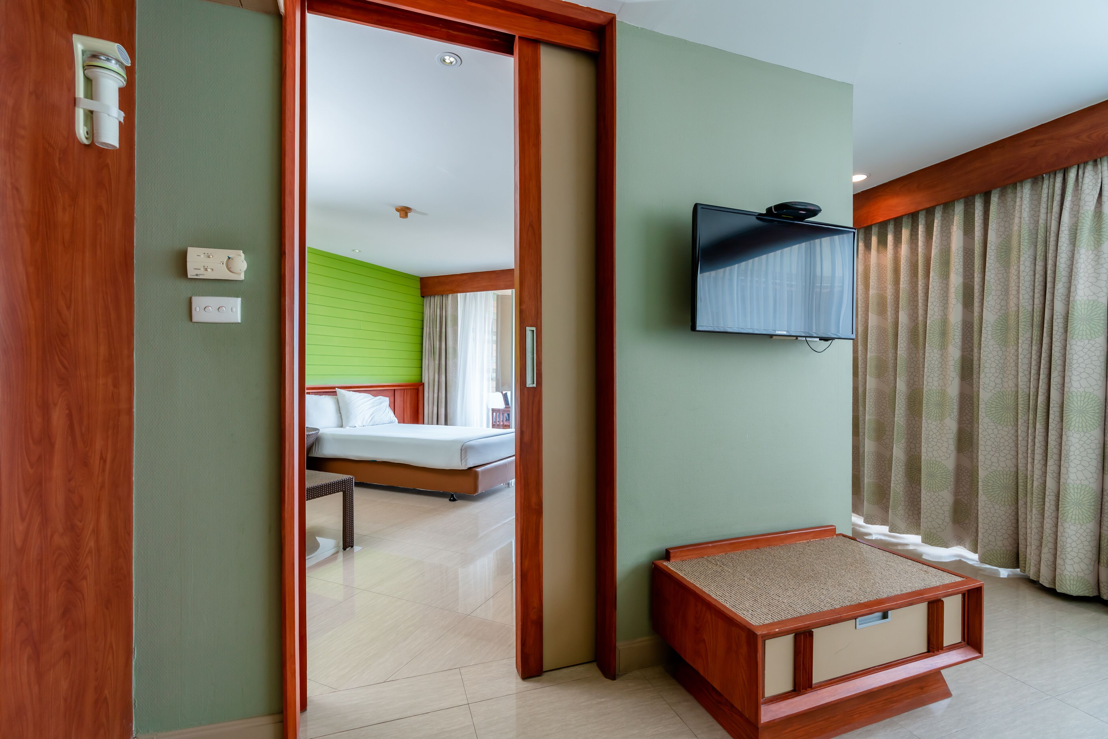A hotel room with a bed, a television mounted on the wall, and a small wooden bench.