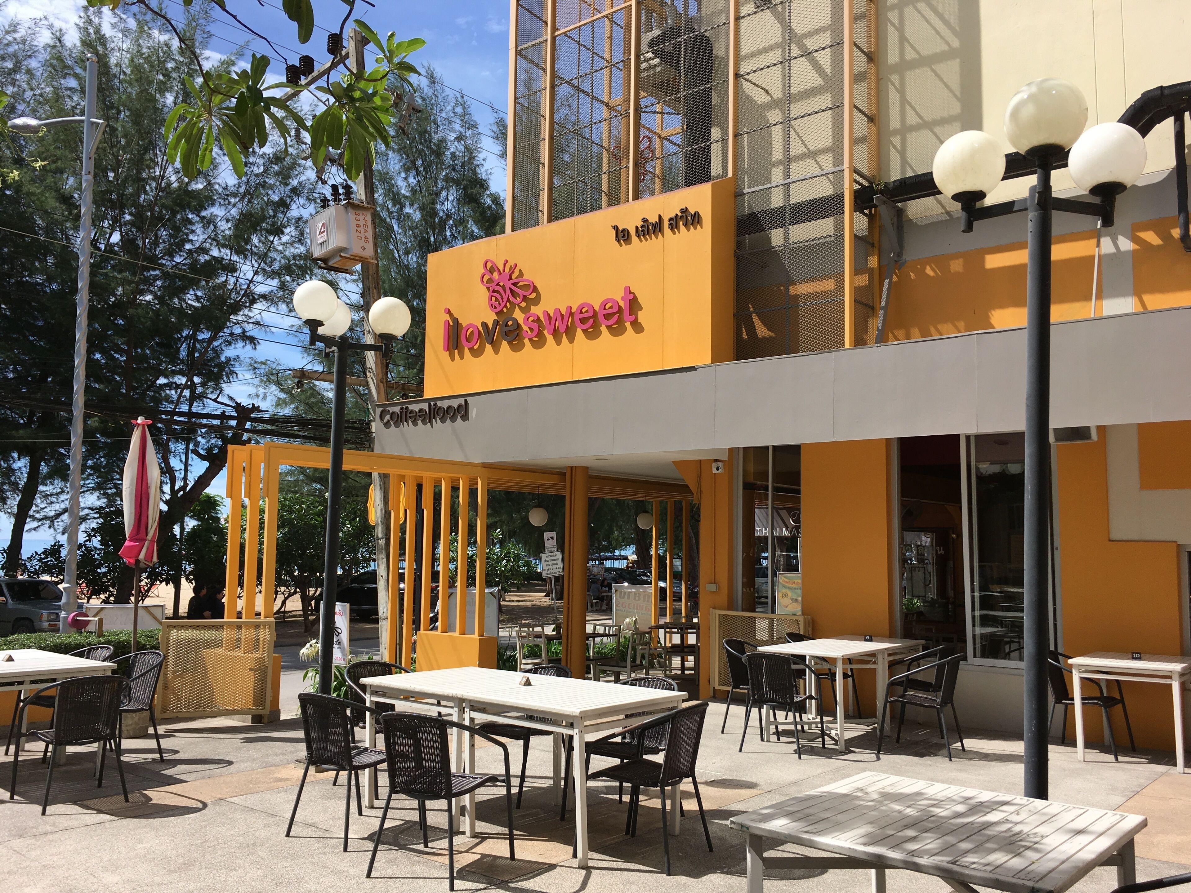 An outdoor seating area with tables and chairs, a yellow awning, and a sign that reads "lovesweet".