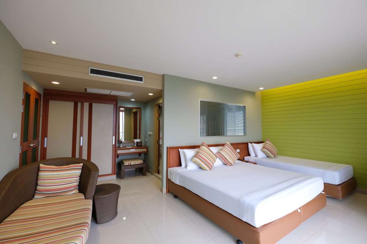 A hotel room with a large bed, a sofa, a small table, and a mirror.