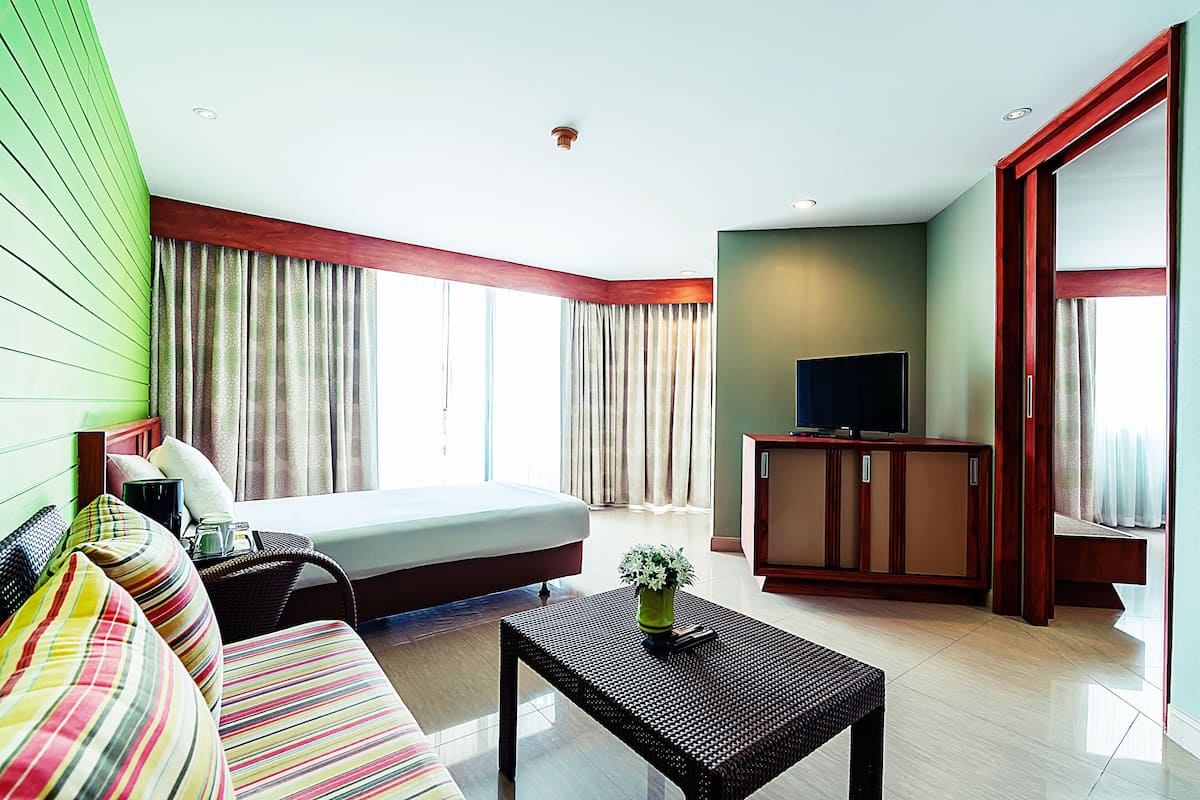 A hotel room with a bed, a sofa, a television, and a cabinet.