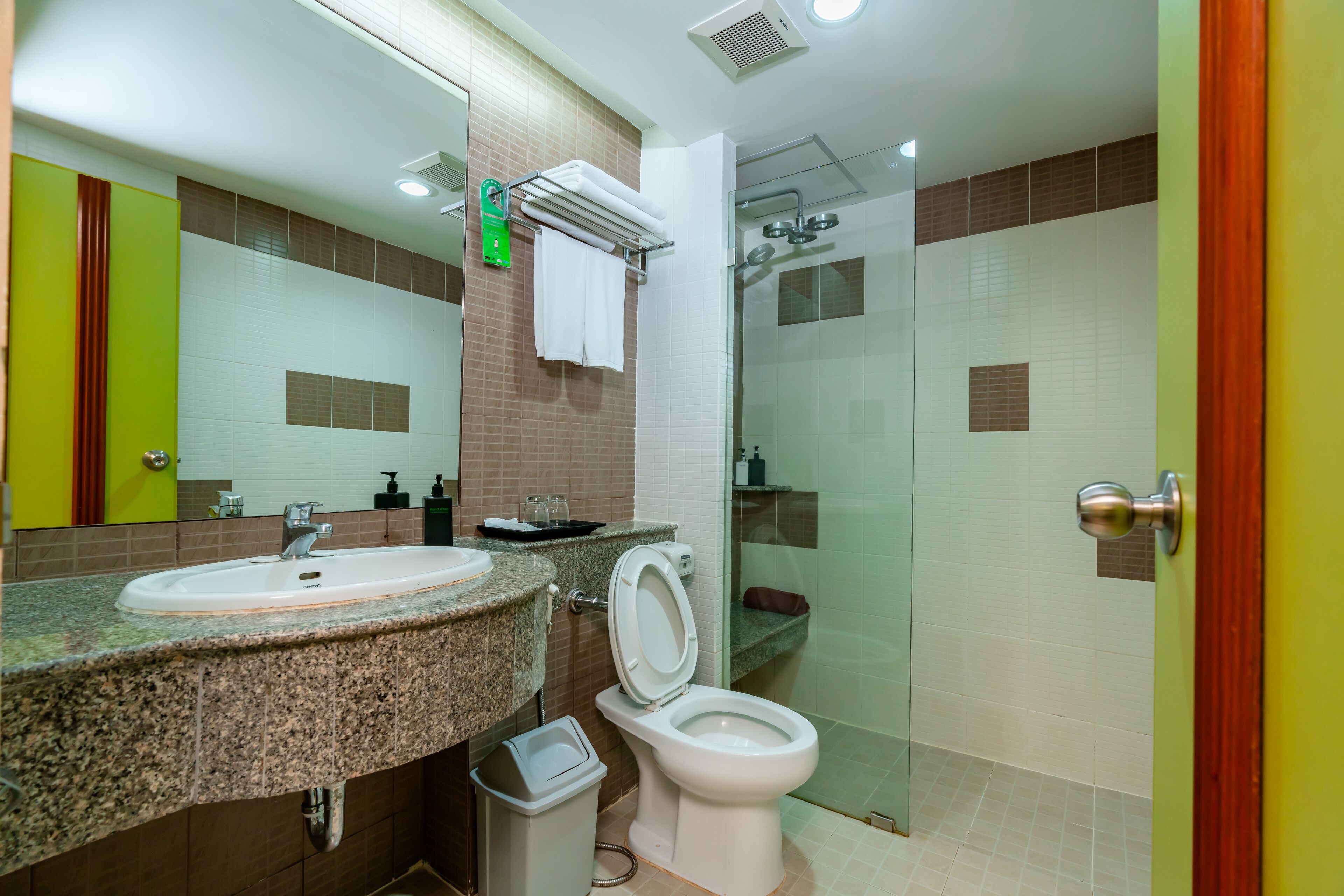 Een moderne badkamer met een wastafel met een granieten blad, een wit toilet en een douche met glazen wanden.