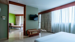 A hotel room with a bed, a television mounted on the wall, a wooden bench, and a view of a balcony with curtains. - Long Beach Cha-Am Hotel (Cha-am)